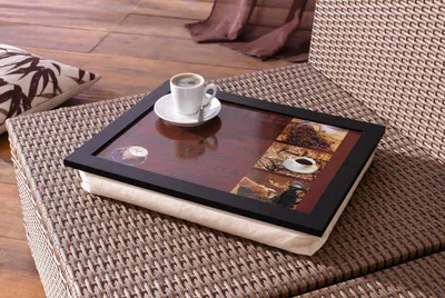A lap tray with a coffee cup and saucer on it, placed on a wicker chair.