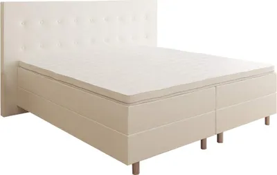 A cream-colored box spring bed with a tufted headboard is shown against a white background.