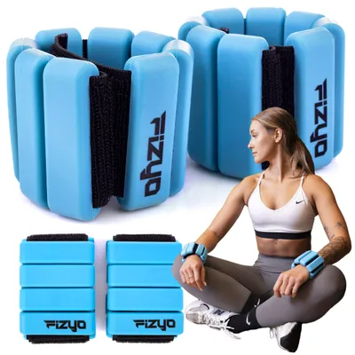 A woman is sitting on the floor wearing ankle weights, with other ankle weights stacked nearby.