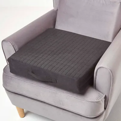 A dark gray orthopedic seat cushion is placed on a light gray armchair.