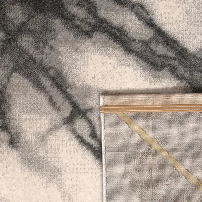 A close-up view of a rug, showing its texture and pattern. The corner of the rug is folded back, revealing the underside.