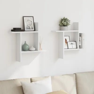Two white wall shelves are mounted on a white wall above a neutral-colored sofa. The shelves are decorated with various items, including framed pictures, vases, and books.