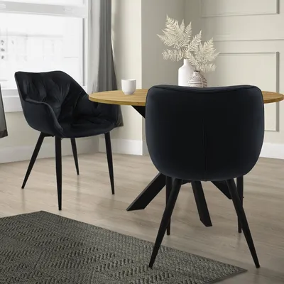 Two black velvet dining chairs are shown around a round wooden table in a dining room setting.