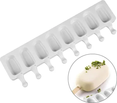 A white silicone ice pop mold with eight cavities is shown on a white background. A close-up inset shows a finished ice pop covered in white chocolate and topped with chopped pistachios.