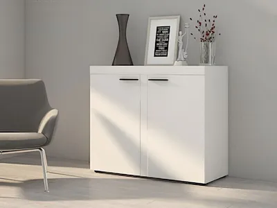 A white cabinet with two doors is shown in a room with a chair and decorative items on top.