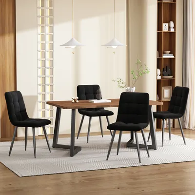 A dining room set with a wooden table and four black chairs on a rug, with a bookshelf and decorative wall feature in the background.