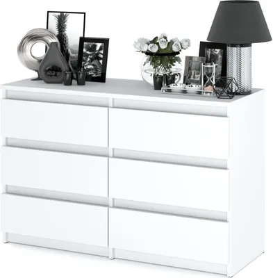 A white dresser with decorative items on top, including framed pictures, a vase of flowers, and a lamp.