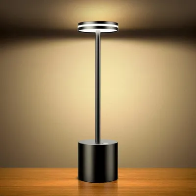 A black LED table lamp with a circular light source is placed on a wooden surface against a gradient brown background.