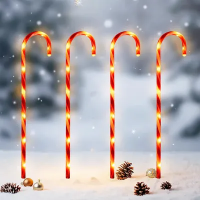 Four illuminated candy canes stand in the snow with pinecones and ornaments.