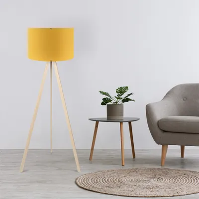 A yellow tripod floor lamp is shown in a room with a gray armchair and a small side table with a plant.