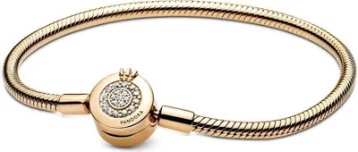 A close-up studio shot of a gold Pandora bracelet with a crown-shaped clasp encrusted with small diamonds.