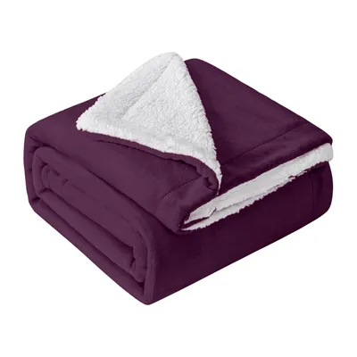 A folded purple sherpa blanket with a white lining is shown against a white background.