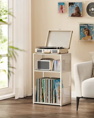 A record player stand with records and a record player on top, placed near a window with sheer curtains.