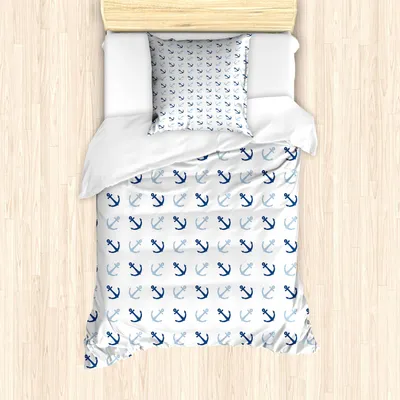 A top-down view of a twin-sized bedding set with an anchor pattern, laid out on a wooden floor.