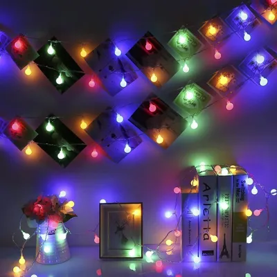 A string of colorful LED lights is draped across a wall, interspersed with diamond-shaped pictures. Below, a vase of flowers and a stack of books are also illuminated by the lights.