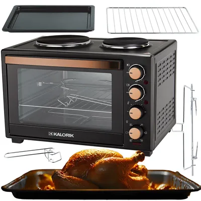 A collection of kitchen appliances and accessories, including a mini oven with hot plates, a baking tray, a wire rack, a rotisserie spit, and a roasted chicken in a baking dish.