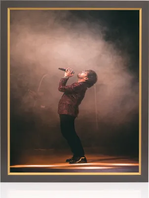 A man singing into a microphone on a stage with smoke and spotlights.