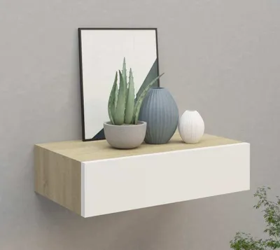 A floating shelf with a drawer, decorated with a framed picture, a potted plant, and two vases.
