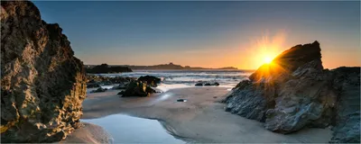 Produktbild von Wallario Poster - Sonnenuntergang hinter einem Felsen am Strand, Kunstdruck Größe: 80 x 200 cm