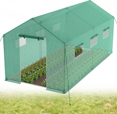 A green greenhouse filled with plants, shown outdoors on a grassy area.