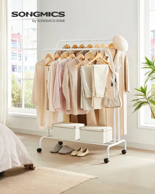 A white garment rack with clothes hanging on it, placed in a room with a window and a bed.