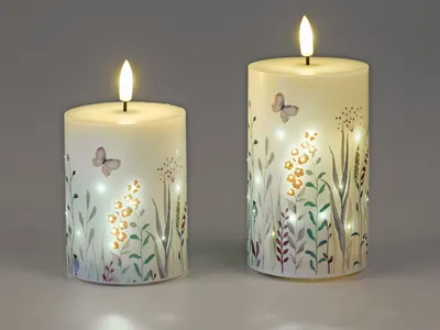 Two LED candles with a floral and butterfly design are displayed against a plain gray background.