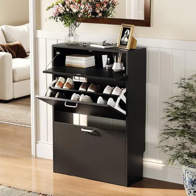 A black shoe cabinet with multiple shelves and drawers, placed in a hallway next to a sofa and a potted plant. The top of the cabinet displays decorative items like a vase of flowers and a framed picture.