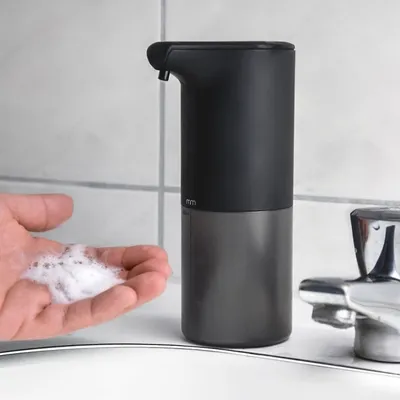 A hand is being foamed by an automatic soap dispenser over a sink.