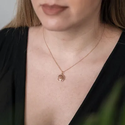 Nahaufnahme von einem Roségold vergoldeten Collier mit filigranem Lebensbaum-Anhänger in rundem Design getragen von einer Frau mit einer weißen Bluse.