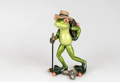 A figurine of a frog dressed as a hiker, complete with a backpack and walking stick, stands on a white background with rocks at its feet.