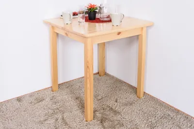 A small wooden table is placed in a corner of a room, on a carpet.