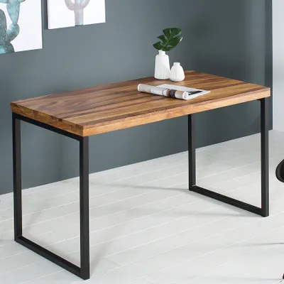 A wooden desk with black metal legs is shown in a room with a gray wall and white floor.