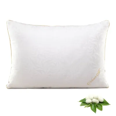 A white pillow with a subtle floral pattern and a small pile of silk cocoons on green leaves in the foreground.