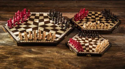 Three hexagonal chess boards with chess pieces arranged for play, set on a wooden surface.