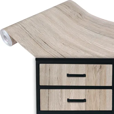 A roll of wood-grain contact paper is shown partially unrolled over the top of a dresser with two drawers.