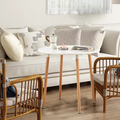 A small white round table with wooden legs is set in a living room area with a sofa and two chairs.