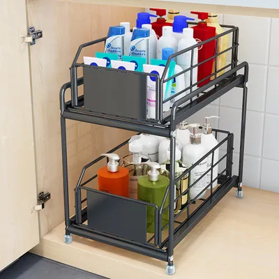 A two-tier sliding storage organizer filled with various bottles of toiletries and cleaning supplies, placed inside a cabinet.