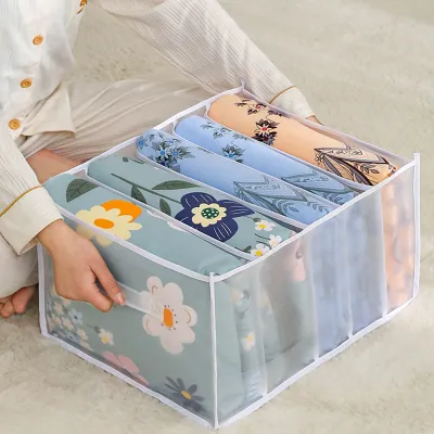 A person is organizing bedding in a fabric storage box with multiple compartments.