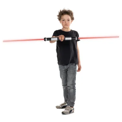 A young boy holds a double-bladed lightsaber horizontally in front of him against a white background.