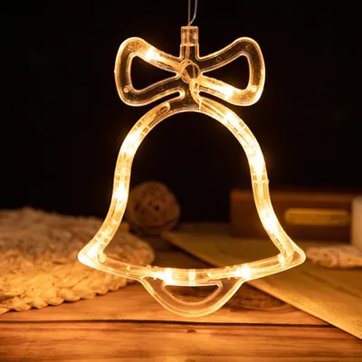 A close-up shot of a bell-shaped LED light decoration hanging against a dark background, with some decorative items in the foreground and background.