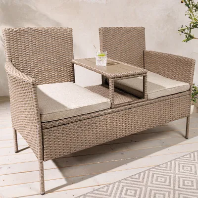 A modern outdoor bench with a built-in table and a drink on it, placed on a wooden deck with a patterned rug.