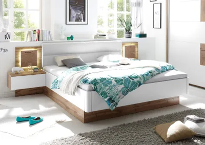 A modern bedroom with a large bed, nightstands, and decor, illuminated by natural light.
