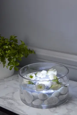 A glass bowl filled with water, white stones, and white flowers, illuminated by LED lights.