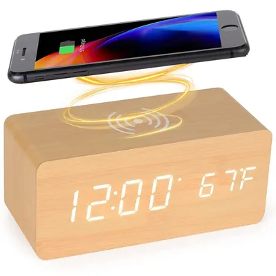 A digital alarm clock with a wooden finish and a smartphone wirelessly charging on top.
