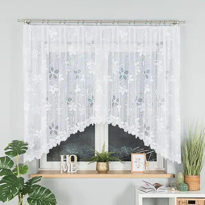 A white lace curtain with a floral pattern hangs over a window. Decorative items are placed on the windowsill below.