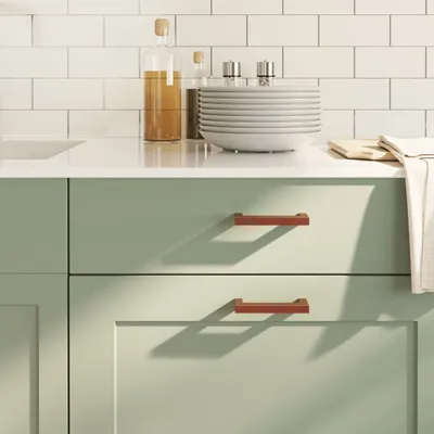 A close-up view of kitchen cabinets with two modern cabinet handles, a stack of plates, and bottles of oil on a countertop.