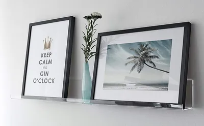 Two framed pictures and a vase with flowers on a shelf.