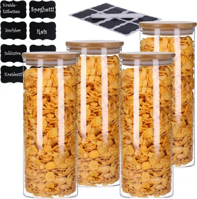 A set of four glass storage jars filled with cereal, with a stack of chalk labels in the background.