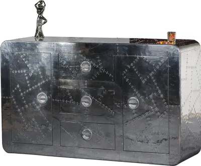 A silver metal sideboard with decorative rivets and round handles, displayed against a white background. A small figurine and a candle are placed on top.