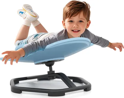 A young boy is lying on a blue sensory swivel chair, with his arms and legs outstretched, as if flying.